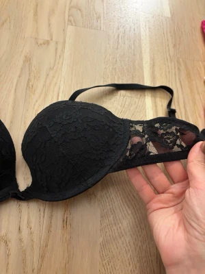 Svart spets-bh från Lindex 75B - Snygg svart bh från Lindex i storlek 75B. Bh:n har vadderade kupor och är täckt med vacker spets framtill samt genomskinliga spetsdetaljer på sidorna. Axelbanden är justerbara för bästa passform. Nästan helt ny använd 2 gånger 