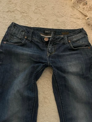 Mörkblå jeans från ONLY - Säljer ett par mörkblå jeans från ONLY med klassisk femficksmodell och snygga slitningar. Jeansen har normal midja, raka ben och detaljer i kopparfärgade nitar. Perfekta till en avslappnad look.