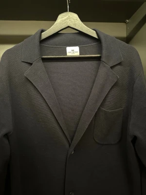 Mörkblå Taupe Stickad Kavaj från John Henric - Säljer en Mörblå Taupe Kavaj från John Henric med klassisk krage och tre framfickor. Koftan har knäppning framtill och är tillverkad i ett stickat material som ger en stilren och chill look. Perfekt att slänga på sig över en t-shirt eller skjorta.