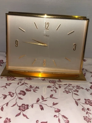 Guldfärgad bordsklocka från Imhof - Stilren bordsklocka från Imhof i guldfärgad metall med rektangulär form. Urtavlan är ljus med guldiga visare och siffror. Perfekt som snygg inredningsdetalj för dig som gillar retrovibbar och klassisk design.