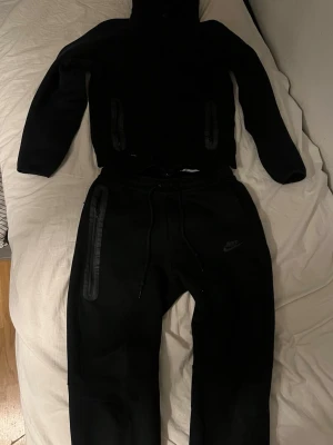 Svarta Nike mjukisbyxor med dragkedjor - Säljer ett par svarta mjukisbyxor från Nike med snygga dragkedjor på sidorna och justerbar midja med snörning. Byxorna har en sportig look och är tillverkade i mjukt material som passar perfekt för chill eller träning. Nike-logga på benet för extra stil.