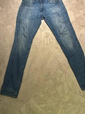 Blå slim fit jeans från replay - Snygga blå slim fit jeans med lätt slitna detaljer och klassisk femficksdesign. Jeansen har normal midja och raka ben. Perfekta till en avslappnad stil och passar till det mesta. Tillverkade i mjukt denimtyg för skön känsla.