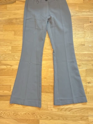 Gråa kostymbyxor - Snygga grå kostymbyxor med utsvängda ben och hög midja. Klassisk design med knapp och dragkedja framtill samt fickor bak. Perfekta för en stilren look. Materialet känns mjukt och har en lätt stretch för extra komfort. Jag är 159 och byxorna är lite korta för mig så skulle säga att dom passar en 157 lång person! Jag har aldrig använt dessa byxor men har ej prislapp kvar!