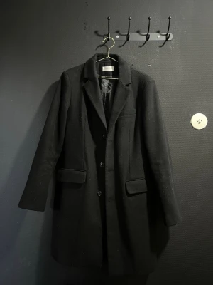 Kappa / Rock från Pier One - Tjena, Stilren svart kappa från Pier One. Klassisk rak modell med tre knappar framtill, två fickor med lock och slät innerfoder. Perfekt för dig som vill ha en tidlös och elegant look. Storlek S och den fri från cigg doft. 