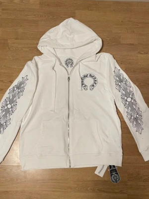 Vit Chrome Hearts Hoodie - Säljer en vit hoodie med dragkedja från Chrome Hearts. Är storlek S men är stor i storleken så passar bättre för storlek M/L. Aldrig använd då den är för stor.