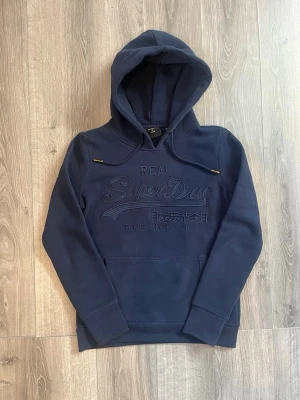 Mörkblå hoodie från Superdry - Snygg mörkblå hoodie från Superdry med broderad logga och japansk text på bröstet🤗 Passar S-Xs inge tecken på fel😇 kan gå ner vi snabbaffär🙌🏻