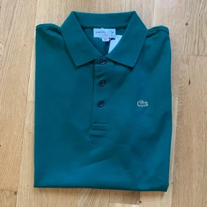 Grön pikétröja från Lacoste - Lacoste Slim Fit Pikétröja i mycket fint skick. Klassisk och stilren modell med smal passform som sitter snyggt på kroppen. Tillverkad i högkvalitativ bomull som är både bekväm och andas bra.   • Storlek: L • Färg: Grön • Skick: Mycket bra, oanvänd   • Nypris: ca 1.200 kr • Pris: 600 kr    Skickas samma arbetsdag! Alltid noggrant paketerad. Hör av dig vid frågor och bilder! Smidiga affärer uppskattas alltid.