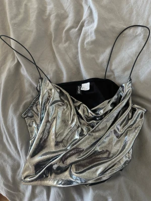 Silver metallic croppad linnetopp - Snygg croppad linnetopp från Divided i metallic silver med tunna axelband och draperad front. Perfekt för dig som vill sticka ut med en glittrig look. Materialet är glansigt och känns mjukt mot huden.