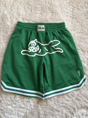 Gröna meshshorts från Icecream - Gröna meshshorts från Icecream med vit grafisk logga framtill och vita/gröna ränder längs bensluten. Shortsen har elastisk midja och avslappnad passform, perfekta för en sportig och chill stil.