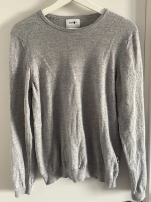 Grå stickad tröja från NN07 - Snygg grå stickad tröja från NN07 med rund halsringning och långa ärmar. Tröjan har en enkel och stilren design med ribbade muddar vid ärmslut och nederkant. Perfekt basplagg i mjukt material.