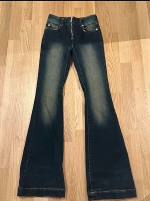 Mörkblå bootcut jeans med dragkedja - Snygga mörkblå bootcut jeans med lätt slitna detaljer framtill och baktill. Jeansen har klassisk femficksmodell, dragkedja och knapp i midjan. Materialet är denim med en skön stretch. Perfekta för dig som gillar retrovibbar och vill ha ett par jeans med utsvängda ben.
