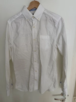 Vit klassisk skjorta med knappar - Klassisk vit skjorta med lång ärm, bröstficka och knappar hela vägen framtill. Skjortan har en stilren krage med knappar och är tillverkad i bomull. Perfekt till både jeans och kostymbyxor.
