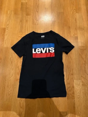Svart Levi's t-shirt med logga - Snygg svart t-shirt från Levi's med den klassiska loggan i vitt, blått och rött framtill. T-shirten har korta ärmar och rund halsringning. Tillverkad i mjuk bomull som är skön att bära hela dagen.