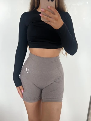 Gymshark träningsshorts - Säljer ett par bruna/gråa högmidjade shorts från Gymshark. De är tighta och har en seamless design med diskret mönster på sidorna och logga framtill. Lappen är bortklippt men uppskattas vara storlek XS/S. Färgen är mest lik den första bilden 🤎