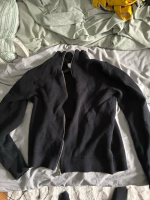 Svart ziptröja från Selected Homme - Säljer en svart stickad ziptröja från Selected Homme. Tröjan har hög krage, dragkedja framtill och ribbade muddar vid ärmslut och nederkant. Perfekt för lager på lager och enkel att matcha med olika outfits.