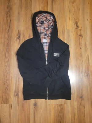 Svart Burberry hoodie med rutigt foder - En storlek M burberry hoodie som är använd men inte skadad. Den är svart med ett rutigt mönster inuti. Jag skickar samma dag! 