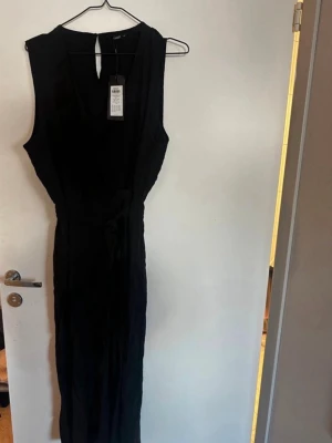 Svart ärmlös jumpsuit från ONLY - Snygg svart ärmlös jumpsuit från ONLY med omlott-ringning och knytband i midjan. Lång modell med smal passform och lätt, mjukt tyg som ger en skön känsla. Perfekt för dig som vill ha en stilren och trendig look. Rök och djurfritt hem. Pruta gärna 🌸