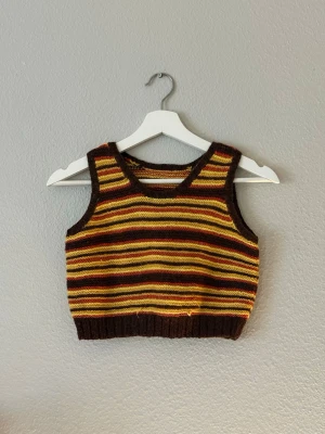 Randig stickad topp - Säljer en stickad topp med breda axelband och rund hals. Toppen har ett randigt mönster i brunt, gult och rött. 