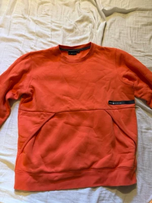 Orange tröja från Sail Racing - En mörkare orange tröja från Sail Racing, storlek 170 (barn) passar även XS möjligen S. Annorlunda ficka på framsidan. Inte använd mycket alls.