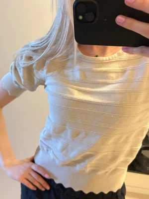 Beige ribbad topp med kort ärm - Snygg beige topp med ribbade horisontella ränder och korta ärmar. Toppen har en rund halsringning och vågig kant nedtill som ger en extra detalj💕