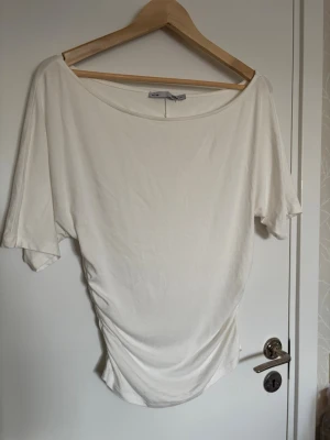 Vit topp från lager 157 - Vit tröja med korta ärmar från Lager 157. Toppen har en bred, rundad halsringning och lätt rynkad detalj i sidan som ger en snygg siluett.