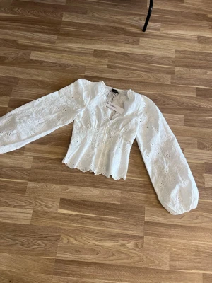 Vit blus från Gina Tricot - Superfin vit blus från Gina Tricot med broderade blommor och knappar framtill. Blusen har v-ringning, markerad midja och långa puffärmar. Tillverkad i ett lätt och luftigt tyg med romantiska detaljer. Slutsåld!