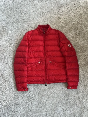 Moncler Agay jacka röd - Hej! Säljer denna perfekta fina moncler jackan i modellen Agay! Jackan är i ett väldigt fint skick i helhet och har mycket fin kvalitet på materialet! Väldigt praktisk jacka som har stora fickor och en ficka på armen, högre krage och krokhängarsnöre har denna också! Jackan har ingen pinhole alls och inga fläckar någonstans och inte inuti som man kanske kan tro när man ser på bild 7. Finns ett enda hål och det syns på 1 och 5e bilden. Enkelt att lägga för😊nypriset ligger på 12k! Hör av dig 🙌