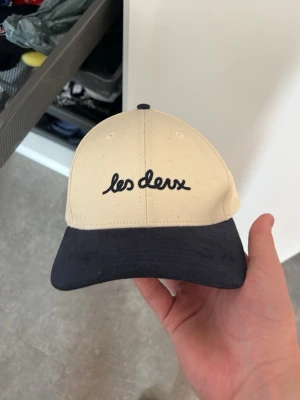 Beige och svart keps från Les Deux - Snygg keps från Les Deux med beige krona och svart skärm. Broderad logotyp framtill i svart. Klassisk form med justerbar baksida. Perfekt för dig som vill ha en stilren accessoar med cool branding. Andvpnt typ 2 gånger ny pris: 550