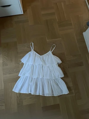 Vit topp med volanger - Söt vit topp med flera volanger och tunna axelband. Toppen har en luftig och flowy passform med v-ringad hals. Perfekt för varma dagar o najs vibe. Materialet känns lätt och somrigt. 