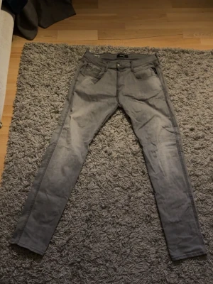 Gråa slim fit jeans Replay Anbass - Snygga gråa slim fit jeans från Replay, modell Anbass. Jeansen har klassisk femficksdesign, dragkedjegylf och är tillverkade i stretchigt material för extra komfort. Perfekta för dig som gillar en modern och smal siluett. W34 L34