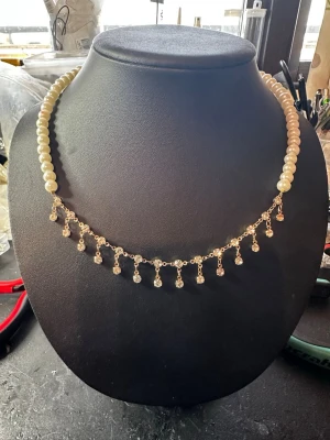 Elegant pärlhalsband med hängande detaljer - Säljer ett elegant halsband med vita pärlor och guldfärgad kedja med små hängande kristall-liknande detaljer. Perfekt för dig som vill ha något unikt och stilrent. Materialet är pärlor och metall, och designen är klassisk med en modern twist.