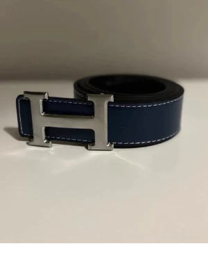 Svart bälte med silverfärgadH-spänne - Snyggt svart bälte med ett ikoniskt H-format silverfärgat spänne. Bältet är gjort i exklusivt skinn med tydliga sömmar längs kanterna och har en stilren, klassisk look som passar till det mesta.