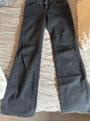 Svarta bootcut jeans med fickor - Säljer ett par svarta bootcut jeans med snygga fickor bak som har lock och silverknappar. Jeansen har klassisk femficksdesign och är tillverkade i denim. Perfekt för dig som gillar en lite vidare passform nertill och cool stil.