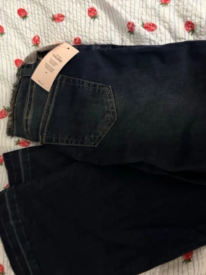 Mörkblå bootcut jeans från Nelly - Säljer ett par mörkblå bootcut jeans från Nelly med klassisk femficksdesign och kontrastsömmar. Jeansen har hög midja och en snygg utsvängd passform som ger en trendig siluett. Perfekta till sneakers eller boots.