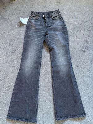 Gråa flared jeans från Weekday - Säljer ett par gråa Glow Curve jeans från Weekday med hög midja och utsvängda ben. Jeansen är tillverkade i en blandning av ekologisk och återvunnen bomull och har en snygg tvättad look. Perfekta för dig som gillar trendiga och bekväma jeans. Helt oanvända med prislappen kvar!    Säljes då de inte kommit till användning 🤍
