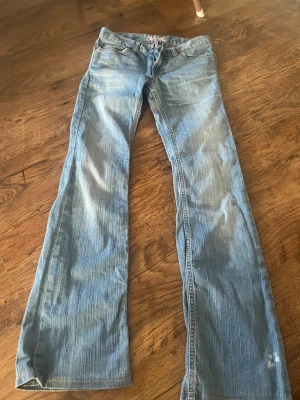 Ljusblå bootcut jeans från Fornairna  - Säljer ett par ljusblå bootcut jeans från Fornarina  med klassiska femficksdetaljer och orangea sömmar. Jeansen har en låg midja och är tillverkade i denim med snyggt slitna partier. Perfekta för dig som gillar en avslappnad och trendig look.