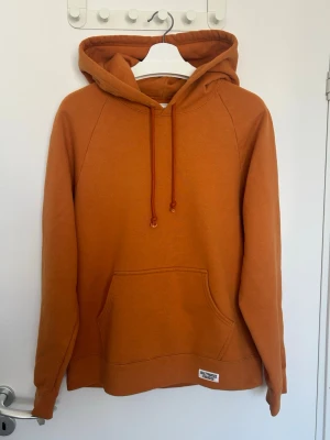 Wacko Maria orange hoodie med grafiskt tryck - Säljer en orange hoodie från Wacko Maria med stor ficka framtill och dragsko i huvan. Baksidan har ett grafiskt tryck av en tecknad figur och japanska tecken. Hoodien är i mjukt bomullsmaterial och har en avslappnad passform. Perfekt för dig som gillar streetwear och unika prints.