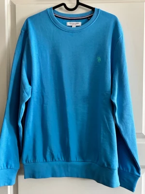 Blå sweatshirt från U.S. Polo Assn - Snygg blå sweatshirt från U.S. Polo Assn med rund halsringning och diskret logga broderad på bröstet. Tröjan har långa ärmar och ribbade muddar vid ärmslut och nederkant. Perfekt för en avslappnad och stilren look.