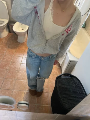 Grå zip-hoodie  - Säljer en grå hoodie med dragkedja, huva och rött tryck på bröstet. Hoodien har ribbade muddar och är i storlek xxs men skulle snarare säga att det är en xs eller s. 