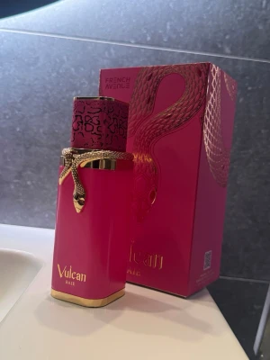 Vulcan Baie parfym French Avenue - Lyxig parfymflaska i starkt rosa med gulddetaljer och en elegant ormdekor runt halsen. Flaskan har ett mönstrat lock i rosa och svart och kommer i en matchande presentförpackning med ormmotiv. Perfekt för dig som gillar unika och snygga parfymer.