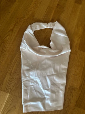 Vit halterneck topp i satin - Säljer en snygg vit halterneck topp i glansigt satinmaterial. Toppen har öppen rygg och knäpps i nacken, vilket ger en elegant och trendig look. Perfekt att styla med jeans eller kjol för en cool outfit.