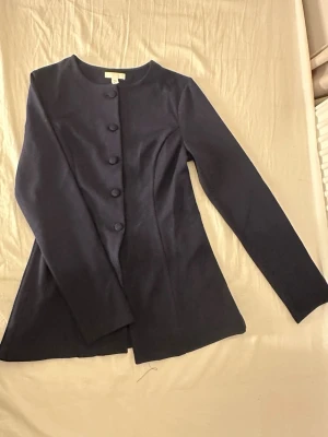 Marinkblå blus från H&M - En figurnära blus i kraftig interlocktrikå med rund halsringning. Blusen har klädda knappar ned till midjan och är lätt utställd från midjan till nederkanten. 