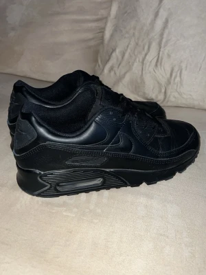 Nike Air Max 90 leather helsvarta sneakers - Säljer ett par helsvarta Nike Air Max 90 sneakers med klassisk chunky sula och ikonisk Swoosh på sidan. Skorna är tillverkade i en mix av läder och syntetmaterial med mesh-detaljer för extra komfort. Grymt stilrena och passar till det mesta. Använda 1 gång