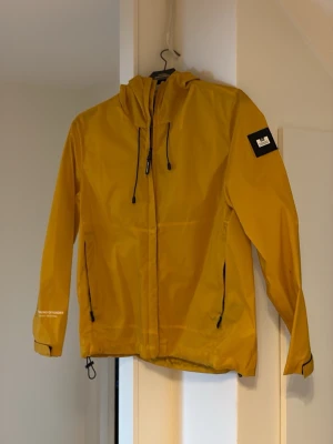 Gul vindjacka från Weekend Offender - Hej, säljer denna snygga gula vind/regn jacka från Weekend Offender i storlek XS. Jackan har en snygg patch på vänster ärm. Har dessvärre en fläck på vänster ärm men annars använd med omsorg och inte andra defekter.