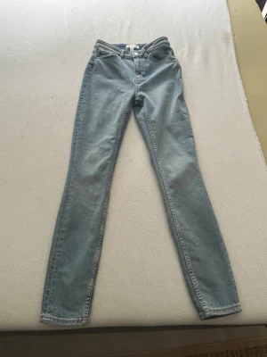 Ljusblå skinny jeans med hög midja - Säljer ett par ljusblå skinny jeans med hög midja och klassisk femficksdesign. Jeansen har smal passform hela vägen ner och är tillverkade i ett mjukt denimtyg. Perfekta för en clean och enkel look.