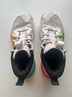 Under armour Embiid one  - Säljer ett par basket skor från Under Armour med vit mesh och coola färgdetaljer i rosa, blått och gult. Skorna har högt skaft, svart innerfoder och vit logga på sidan. Perfekt för dig som vill ha stil på planen!