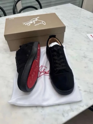 Svarta Louboutin sneakers med röd sula - Snygga svarta sneakers från Christian Louboutin i mocka med klassisk röd sula. Skorna har svarta skosnören, låg profil och diskret logga på sidan. Perfekta för dig som vill sticka ut med en exklusiv touch och ikonisk design.