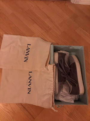 Grå sneakers från Lanvin i mocka - Snygga grå sneakers från Lanvin med ovandel i mocka och detaljer i blankt läder. Skorna har klassisk låg profil, vita sulor och matchande grå skosnören. Perfekta för dig som vill ha en stilren och exklusiv look. Skorna är uk 5, eu 39 men sitter på foten som en 40,5-41. Skicka om ni har några frågor så svarar jag fort!