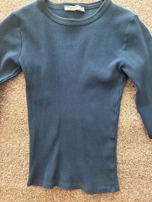 Långärmad tröja - Säljer en blå ribbad långärmad topp från Stradivarius. Toppen har en rund halsringning och är tillverkad i ett stretchigt, mjukt material som sitter tajt mot kroppen. Perfekt att styla med jeans eller kjol för en enkel och snygg look.