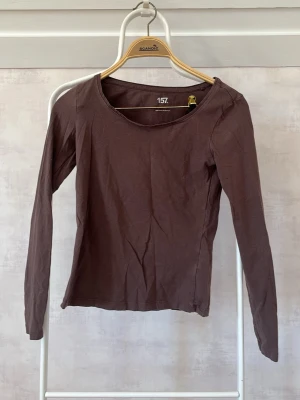Brun långärmad topp från 157 - En enkel brun långärmad topp från 157 med rund halsringning. Tillverkad i mjuk bomull som känns skön mot huden. Passformen är normal och toppen är perfekt att styla lager på lager eller bära som den är.